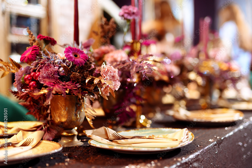 Elegant table set with glasses decorated in gold, lighted candles and rose flowers. Selected focus and blurred background