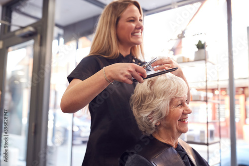 Senior Woman Having Hair Cut By Female Stylist In Hairdressing Salon