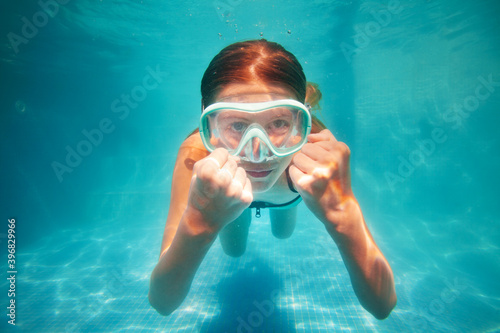 Beautiful underwater portrait of the smiling little girl wearing scuba mask show hands gesture
