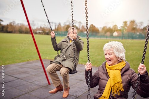 Senior Couple Having Fun Playing On Swings In Park Playground