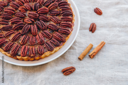 Delicious freshly baked homemade pecan pie on white tablecloth, close up. Sweet food from above. Popular holiday meal for Thanksgiving and Christmas.