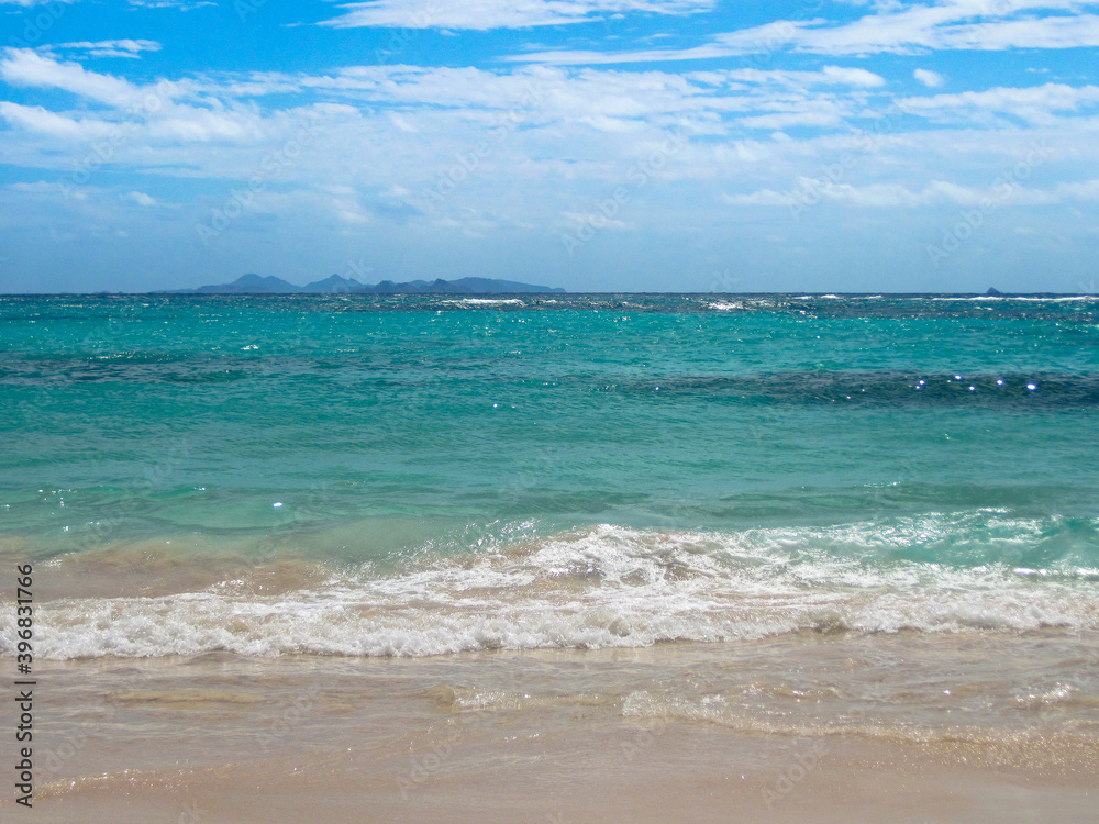 A tropical seascape with white water breaking on sand beach and turquoise sea and distant Caribbean Island in distance A tropical seascape with white water breaking on sand beach and turquoise sea and distant Caribbean Island in distance