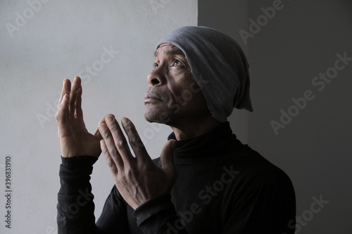 man praying to god with hands together Caribbean man praying with grey background stock photo