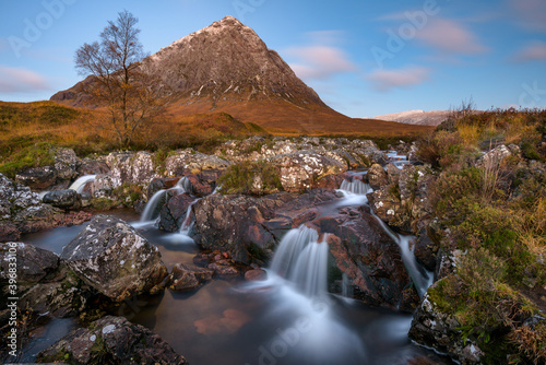 Beautiful Scotland waterfall with blue sky and snowcapped mountain. Taken at Buachaille Etive mor, Glencoe, Scottish Highlands.