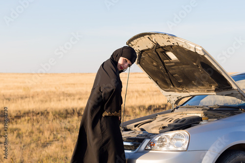 Muslim woman near open hood of car empty road