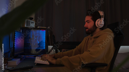 Male using PC and concentrating while wearing white headphones in a darkened room