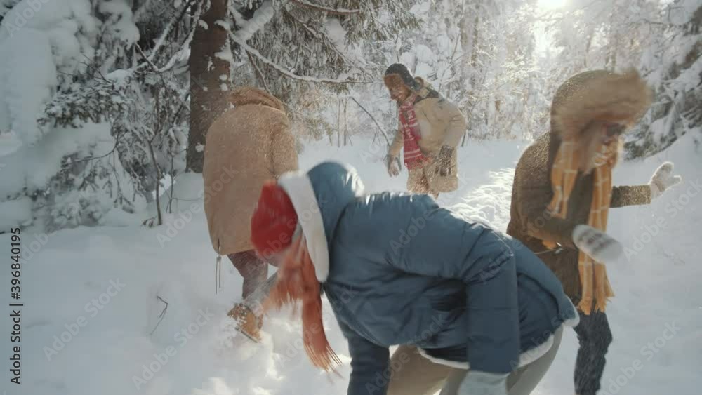 Company of young male and female friends playing snowballs and throwing snow while having fun in forest on sunny winter day