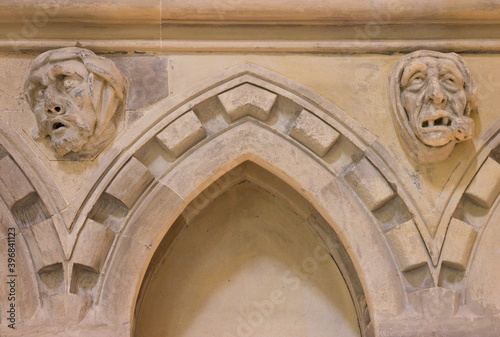 Medieval design. Strange old walled up door with human faces on an ancient stone wall. Facial expression of two weird men: curiosity and suffering of toothache. UK, The Templar Church, 12th century.