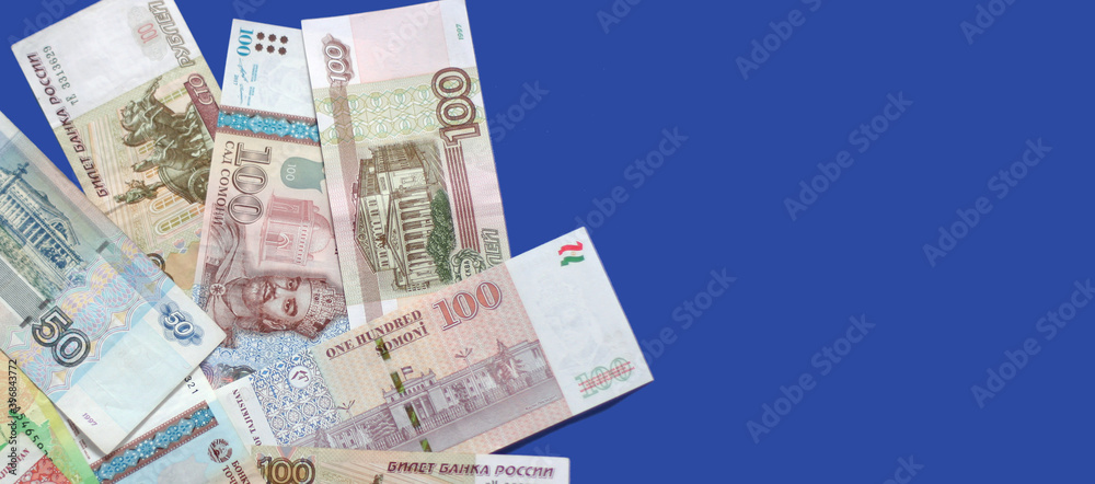 Photo of somoni bank notes from Tajikistan and Russian ruble bank notes on blue background. Banner size, copy space. Focus on money