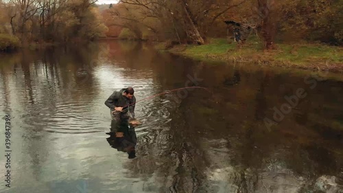 Aerial Dolly In Shot Fisherman Pick Up Grayling Fish and Pose for Camera photo