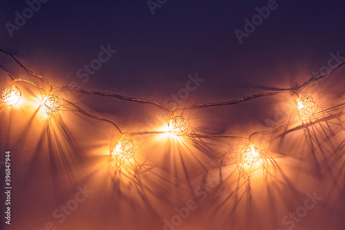Christmas garland of wire in the form of balls with yellow lights with beautiful shadows glows in the dark hanging on the wall. background gradient from purple to yellow