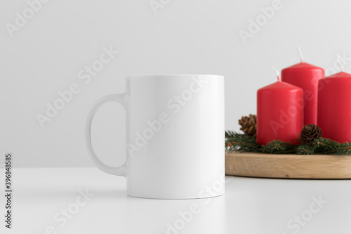 White mug mockup with candles on a table. Christmas decoration