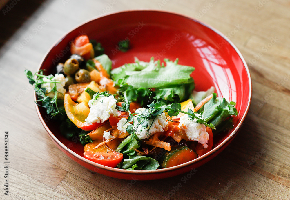 Salad with vegetables and soft Buch cheese in a red plate on a wooden table. Salad with vegetables and soft Buch cheese in a red plate on a wooden table.