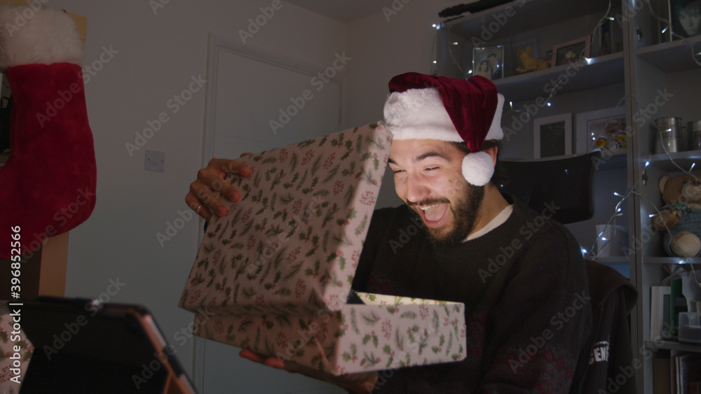 Shocked man opening a Christmas present which lights up while wearing a Christmas hat	
