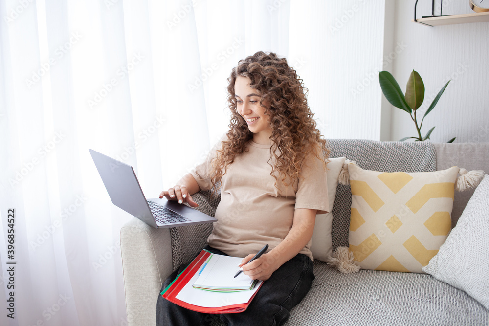 Expectant mother sits comfortably on the sofa, writing a list of the