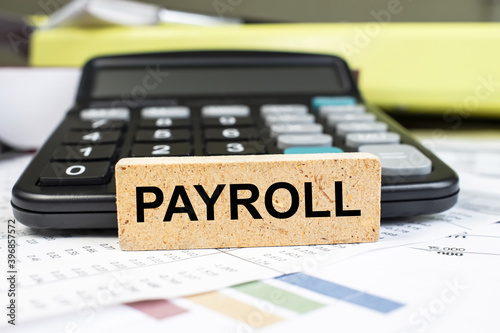 payroll is written on a wooden cube that stands on the documents next to the calculator . Business concept photo