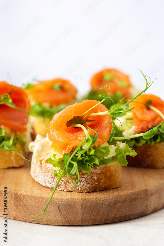 Canapes with mozzarella cheese, salad, salmon and pea sprouts, toast with red fish on a wooden board close up