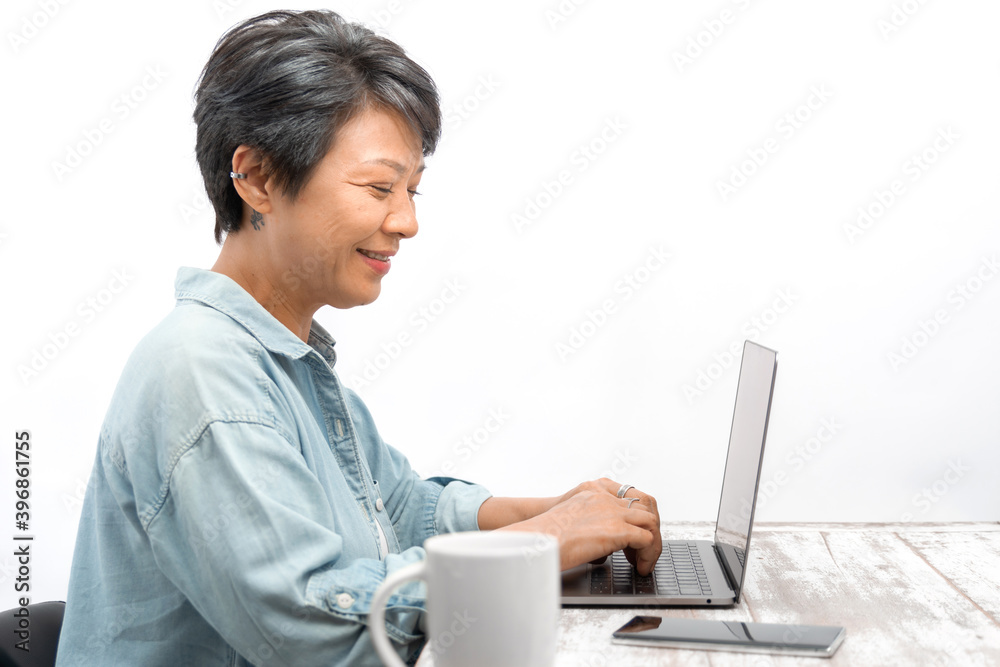 Senior Designer woman working or shopping online on a laptop in office. Asian mature female looking and smiling at the laptop computer while sitting at her desk. Elderly online technology concept Senior Designer woman working or shopping online on a laptop in office. Asian mature female looking and smiling at the laptop computer while sitting at her desk. Elderly online technology concept