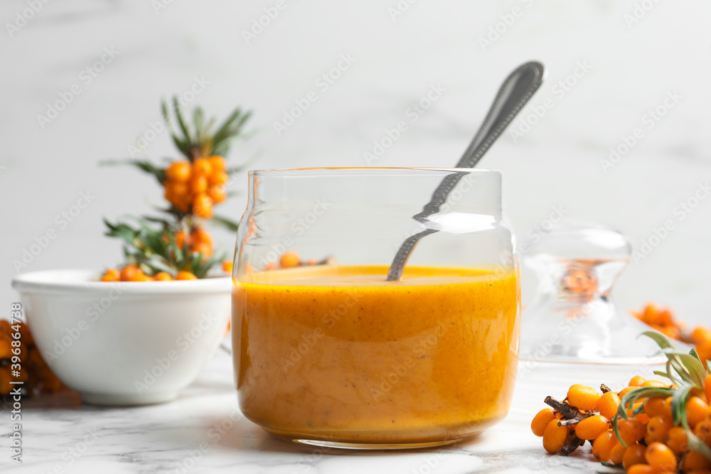 Delicious sea buckthorn jam and fresh berries on white marble table Delicious sea buckthorn jam and fresh berries on white marble table