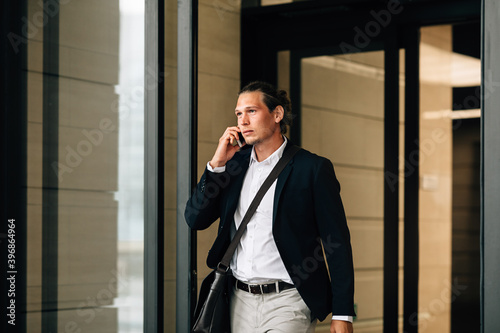 Confident businessman talking on a smartphone while exiting from an office building