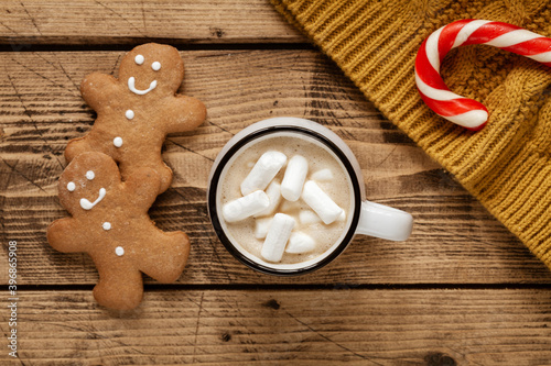 Cup of hot cocoa with marshmallow, gingerbread men and christmas cane on wooden background. Hygge concept