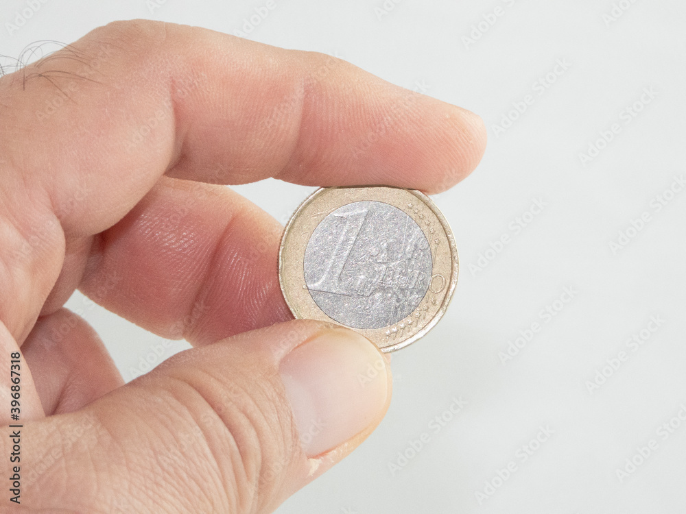 Palma de Mallorca, Spain, November 29, 2020: An adult man's hand holding a 1 euro coin isolated on white background. Illustrative editorial image. Palma de Mallorca, Spain, November 29, 2020: An adult man's hand holding a 1 euro coin isolated on white background. Illustrative editorial image.
