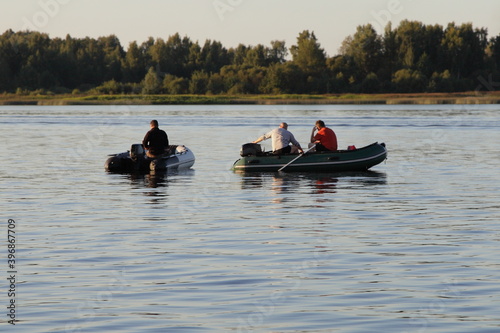 Fisherman people on two PVC inflatable motor boats on river against the background of the far Bank with a green forest on the horizon on a summer morning, fishing on the river