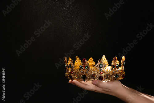 Woman holding beautiful golden crown on black background, closeup with space for text. Fantasy item photo