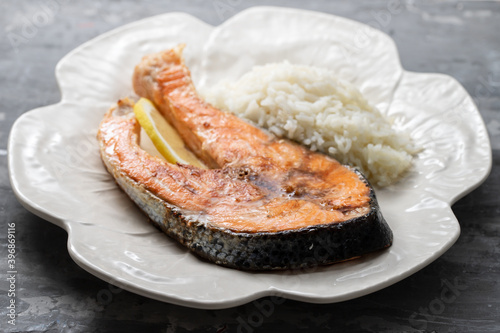 fried salmon with lemon and boiled rice on white beautiful dish on ceramic background