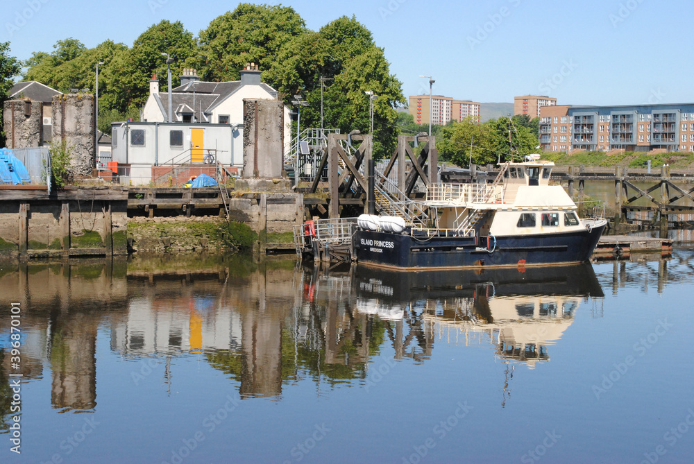 Blue Sky and Reflections of Boat & riverside Buildings and Jetty in Still River Waters