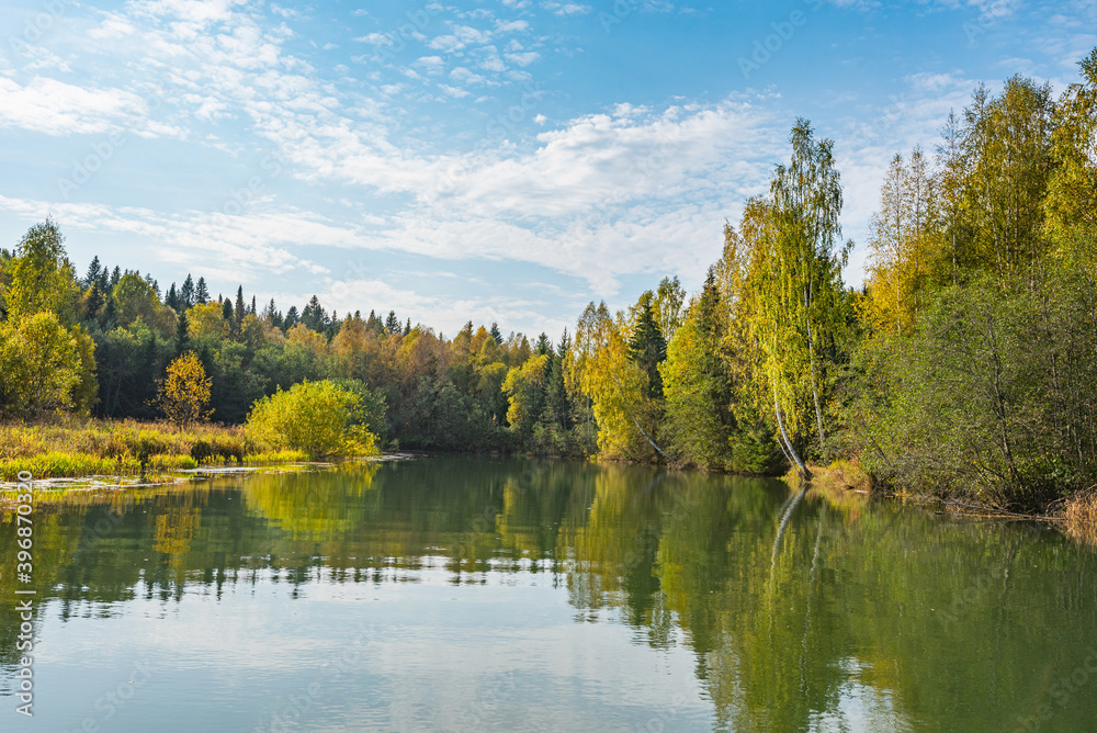 Autumn forest trees are reflected in the river water of the panoramic landscape. Blue sky with clouds. Autumn forest trees are reflected in the river water of the panoramic landscape. Blue sky with clouds.