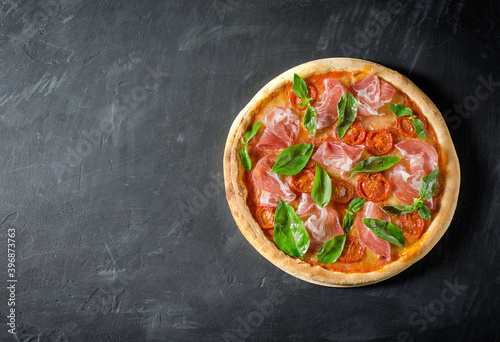 Top view to Italian pizza with prosciutto, tomato, mozzarella on a black board with copy space