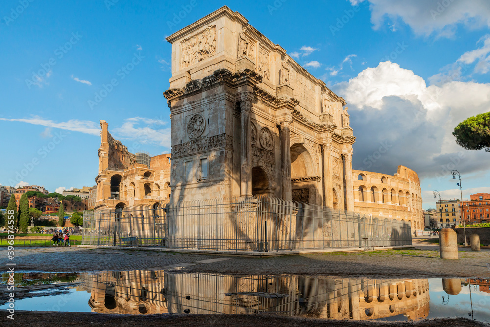 Arch of Constantine near the Colosseum and the Arch of Titus. Photographed after the storm, reflecting in a puddle with few tourists, blue sky and clouds. Rome.