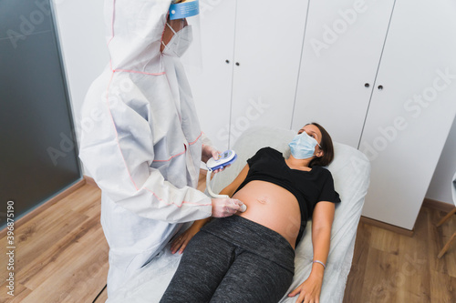 A gynecologist examines a pregnant woman during a Covid 19 pandemic. Fetal doppler heart auscultation. photo