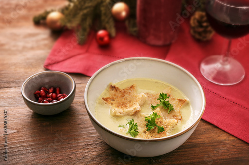 Holiday cream soup with croutons in star shape, parsley garnish and pomegranate seeds, Christmas decoration and a red napkin on a dark rustic wooden table, selected focus