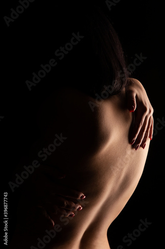 Nude female torso on black background shot from behind. Muscular female back. 