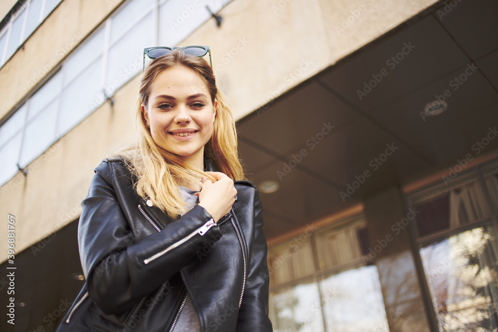 A blonde woman in a leather jacket are walking on the street in the city near the building A blonde woman in a leather jacket are walking on the street in the city near the building