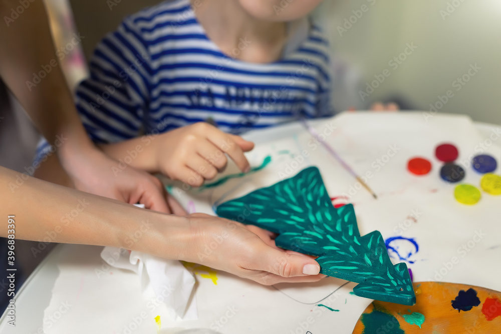 Mother and child together making new year christmas wooden natural vintage fir tree toy painting green color. Happy kid doing handmade xmas art decoration concept. Children diy hobby at home Mother and child together making new year christmas wooden natural vintage fir tree toy painting green color. Happy kid doing handmade xmas art decoration concept. Children diy hobby at home