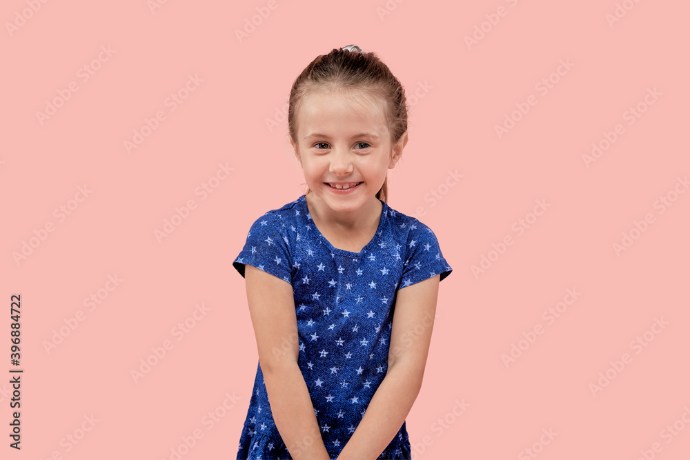 Beautiful happy girl smiles and looks at the camera. In a blue dress with a small star print. Pink isolated background. Beautiful happy girl smiles and looks at the camera. In a blue dress with a small star print. Pink isolated background.