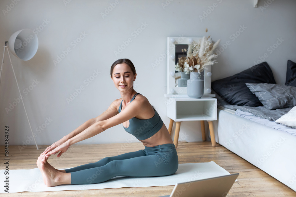 Quarantine sport at home. Young woman practicing fitness stretching exercises online training on laptop