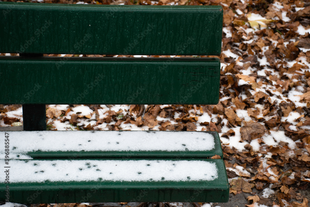 Light snow on a green park bench and autumn leaves on the ground Light snow on a green park bench and autumn leaves on the ground