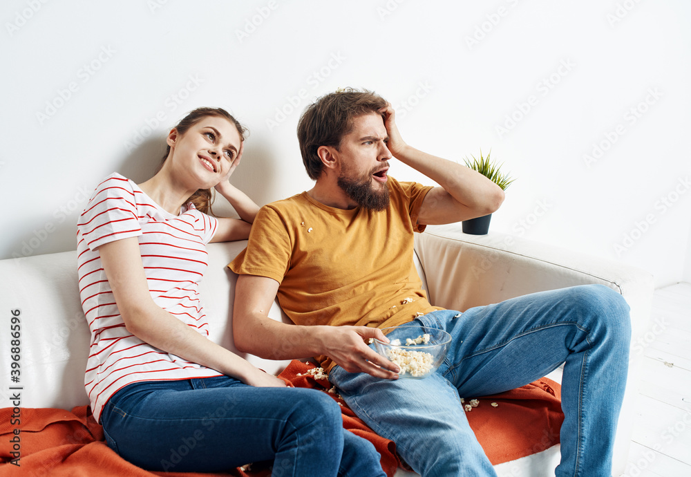 Man with plates popcorn and woman on orange plaid sofa family friends having fun Man with plates popcorn and woman on orange plaid sofa family friends having fun