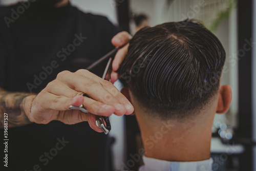 detail of a young man with tattooed arms cuts a man s hair in a barber shop