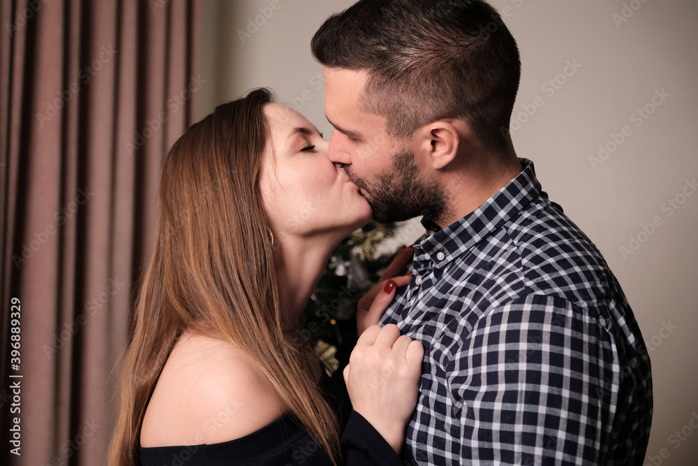 A young woman and a man are kissing while in the room. Christmas and new year celebrations. A young woman and a man are kissing while in the room. Christmas and new year celebrations.