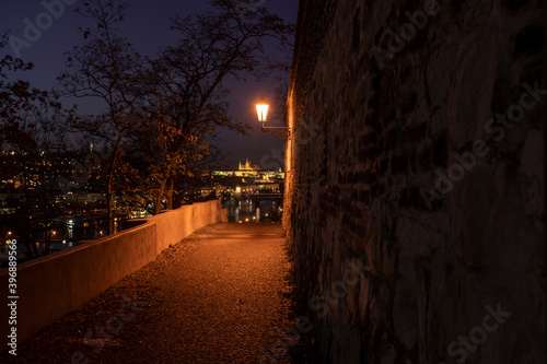 Photography view through the old illuminated defocused stone wall from the 17 century and the light of street lighting and in the background the illuminated Prague Castle and the Church of St