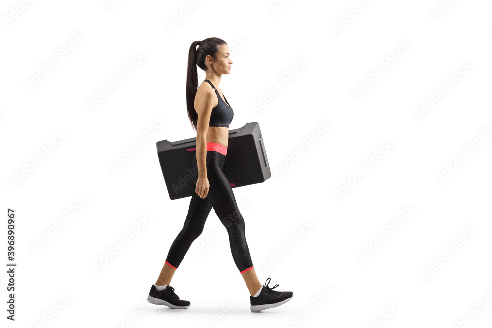 Full length profile shot of a young woman walking and carrying a step aerobic platofrm Full length profile shot of a young woman walking and carrying a step aerobic platofrm