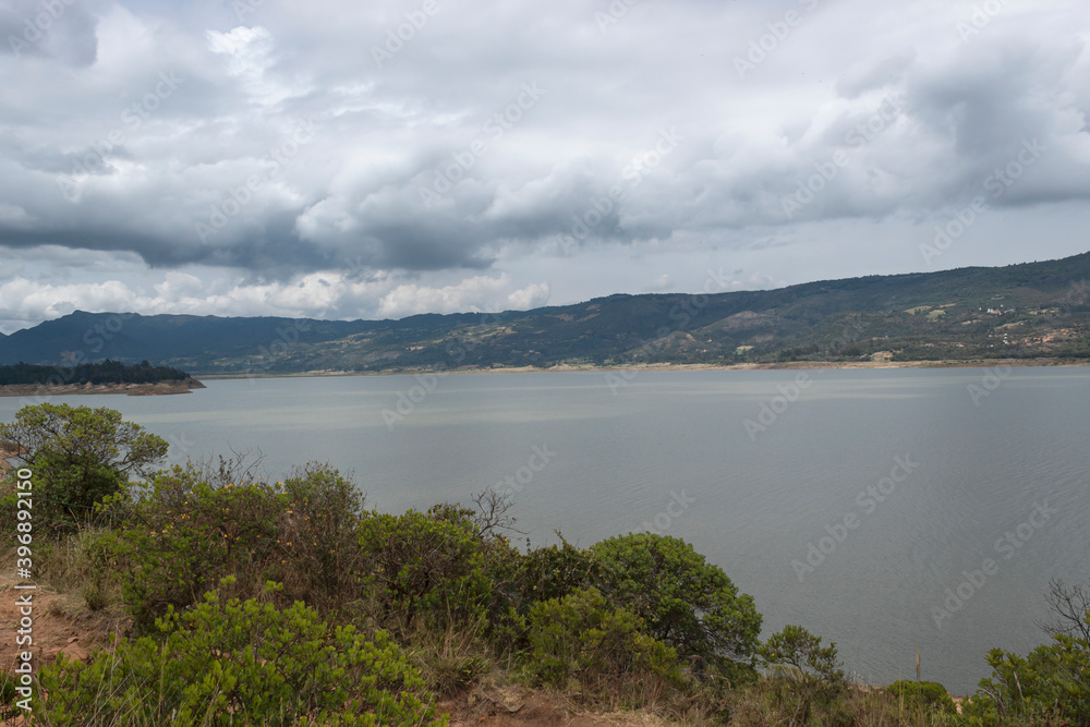 Colombian tomine lake  with green mountains grey clouds and sky refflection at grey day. 