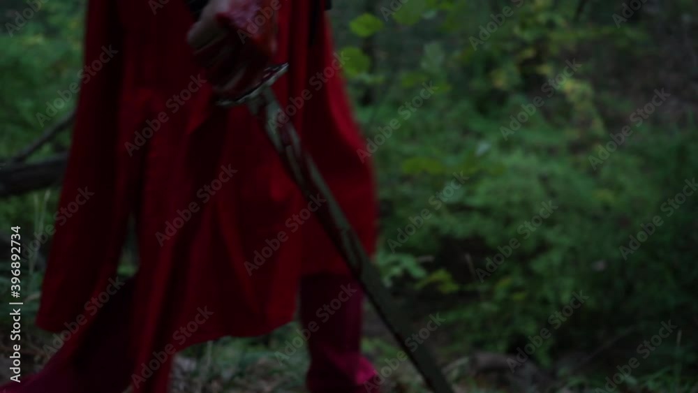 Bloody hand and sword of warrior in red kimono walking through the forest. Cosplay person with fake blood Bloody hand and sword of warrior in red kimono walking through the forest. Cosplay person with fake blood