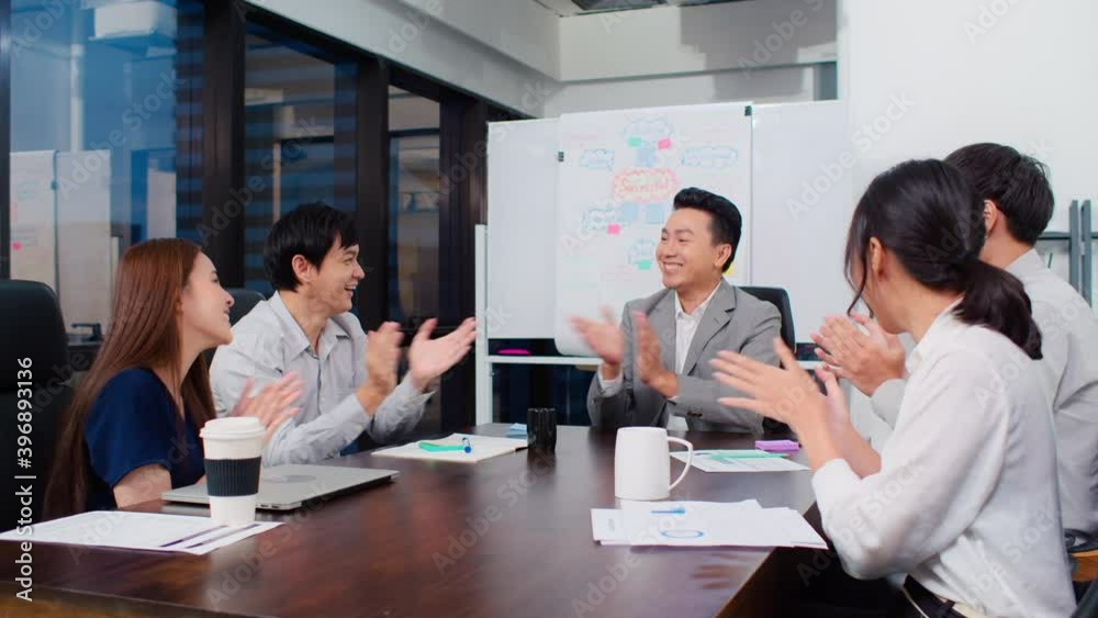 Group of happy Asian business people discuss together in team brainstorm meeting and clap hand, work late night in office. Corporate business, coworker teamwork, or project success celebration concept Group of happy Asian business people discuss together in team brainstorm meeting and clap hand, work late night in office. Corporate business, coworker teamwork, or project success celebration concept