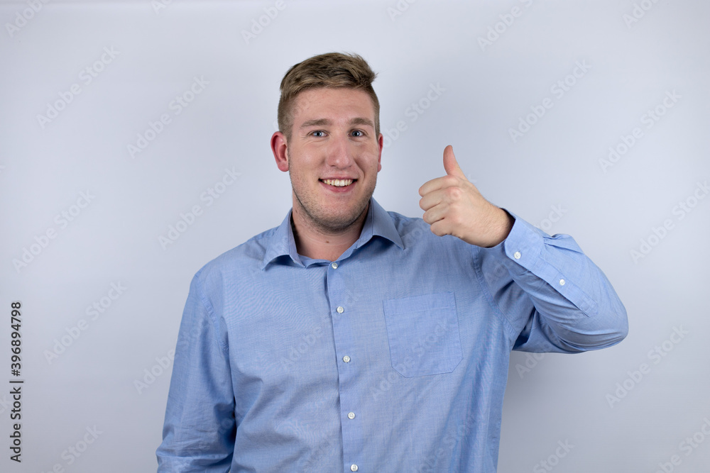 Business young man wearing a casual shirt over white background smiling confident doing ok signal with thumbs Business young man wearing a casual shirt over white background smiling confident doing ok signal with thumbs